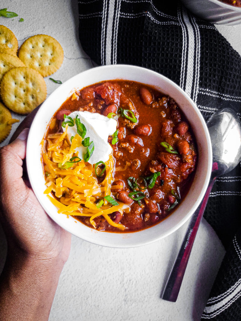 Overhead shot of a bowl of beef chili with shredded cheese and sour cream